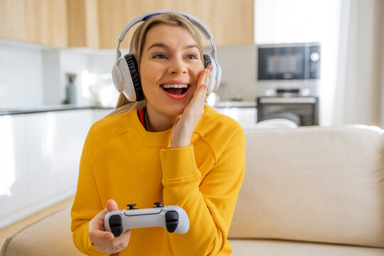 Joyful woman enjoying console gaming with headphones in a cozy home setting