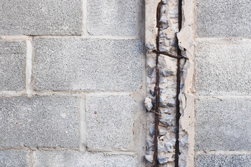 section of a concrete block wall with a vertical crack or gap. The gap reveals the internal structure of the wall, including exposed rebar (reinforcing steel bars) and broken concrete.