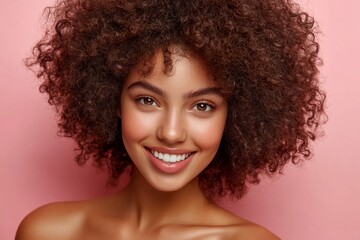 Studio portrait of attractive young woman with perfect teeth and curly hair smiling on pink background