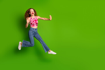 Playful woman jumping against green backdrop in colorful attire