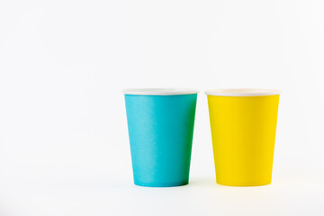 on white background two paper cups for coffee and tea painted in yellow and blue disposable tableware attributes for trips, recreation and picnics eco cups waterproof