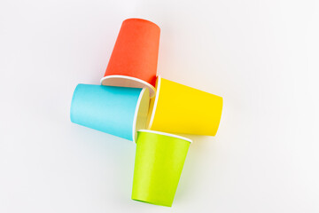 top shot white background lie four paper cups for coffee and tea painted in red, green, yellow and blue colors disposable tableware attributes for trips, recreation and picnics eco cups waterproof