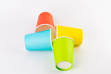 white background lie four paper cups for coffee and tea painted in red, green, yellow and blue colors disposable tableware attributes for trips, recreation and picnics eco cups waterproof