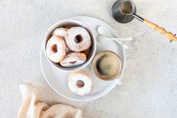 Delicious homemade donuts with sugar and a cup of coffee on a white stone background.