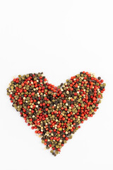 closeup white background a pile of mixed large aromatic peppers black red and white the main seasoning for food peppercorns indian and european spices pepper laid out in the shape of a heart