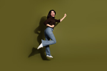 Confident young woman smiling and jumping against khaki background wearing casual attire