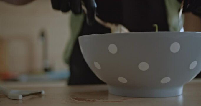 A man wearing black gloves mixes a fresh, healthy salad in a gray bowl with white polka dots.
