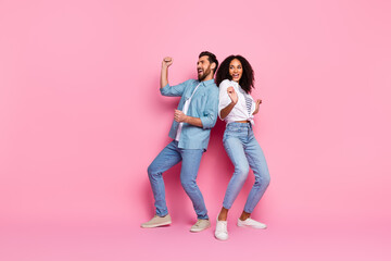 Young happy couple dancing joyfully together against a vibrant pink background while dressed in...