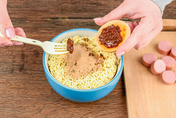 A woman spoons sauce from a saucer on instant noodles using a fork.