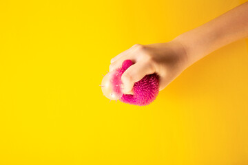 Child hand squeeze pink stress ball on yellow background. Positive thinking concept. Copy space
