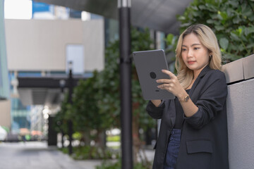 Professional woman holding a tablet in a modern urban setting surrounded by skyscrapers, showcasing confidence, technology, and adaptability in a sleek and innovative environment.