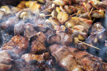 Close-up of many pieces of meat grilling on a barbecue outside. Lots of meat on the barbecue with smoke in a distinct texture. Street food festival.