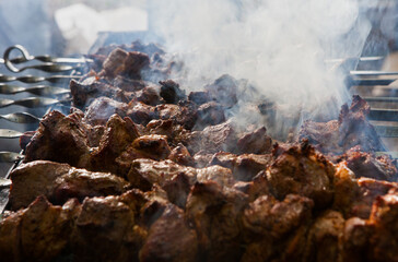 Close-up of many pieces of meat grilling on a barbecue outside. Lots of meat on the barbecue with smoke in a distinct texture. Street food festival.