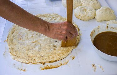 Baker's hands pressing dough on a white counter, with spices and other ingredients in bowls.