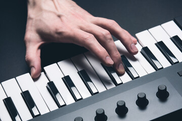 A midi keyboard with a man's hand playing it, piano keys.