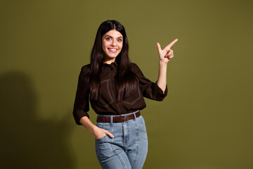Confident young woman with brunette hair pointing to the side against a khaki background