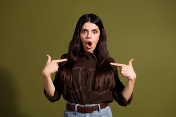 Surprised young woman in a brown shirt pointing at herself against a khaki background