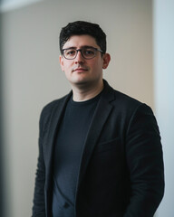 Obraz premium Young businessman in black blazer and glasses against neutral background