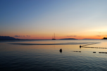 Fototapeta premium Serene sunset over calm waters a sailboat silhouetted against the vibrant sky
