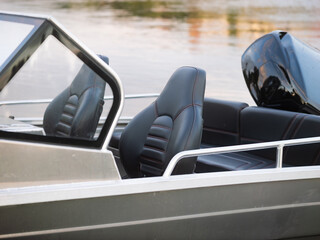 Sport boat with empty seats close-up. Aluminum vessel in a river or lake. Motor boat with an outboard engine and dark leather interior.
