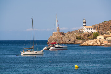 Two elegant yachts drift on calm sea in front lighthouse in Port de Soller, Mallorca. Sun illuminates coastline. Warm atmosphere relaxation, sea travel