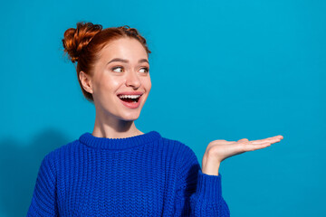 Smiling young woman in blue sweater posing with open hand gesture against bright background