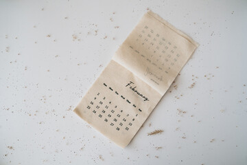 Beige linen fabric calendar with February month 2025 on a white background with copy space. Flat lay, template. Minimal top view aesthetic composition