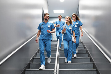 Group of healthcare professionals walking down stairs in hospital hallway.
