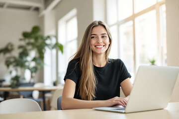 Fototapeta premium Woman smiling while working on a laptop in a modern office setting.