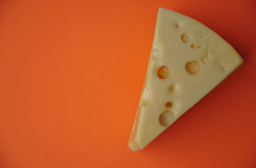 piece of hard cheese with holes on an orange background. dark photo