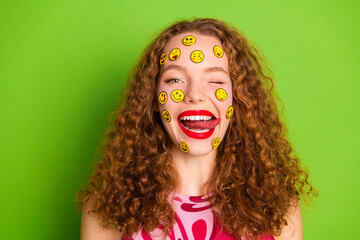 Young woman with curly hair winking and smiling, covered in happy emoji stickers against green