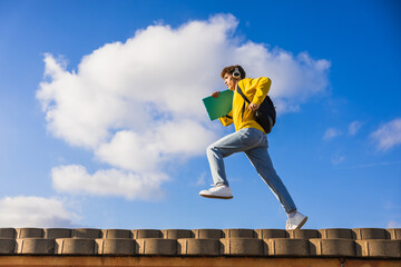 College student running on roof listening music with headphones and holding book
