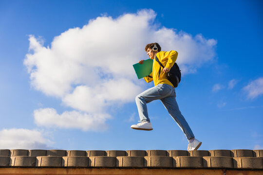 College student running on roof listening music with headphones and holding book