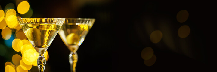 A close-up of a martini glass with a floating olive, set against a background of blurred golden holiday lights, creating a refined and celebratory atmosphere.