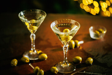 A classic martini glasses with a green olive, standing on a reflective surface with a warm golden holiday glow in the background, creating a rich and festive atmosphere.
