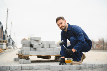 The master in gloves lays paving stones in layers. Laying gray concrete paving slabs in house courtyard on sand foundation base
