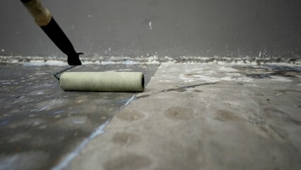 Worker applying waterproofing membrane to concrete floor using paint roller
