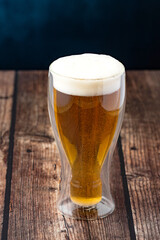 Close-up of golden craft beer with foam in glass on rustic wooden table
