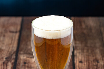 Close-up of golden craft beer with foam in glass on rustic wooden table