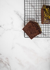 Sliced cake on a cooling rack with a bigger cake on the side. White marble counter as a background