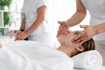 Serene modern daylight ambiance of spa salon, couple customer indulges in rejuvenating with facial skincare mask. Facial skin treatment and beauty cosmetology procedure for face. Quiescent