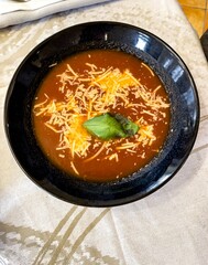 A plate of tomato soup on a white tablecloth. The soup has shredded cheddar cheese.