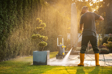 Professional Gardener Uses Pressure Washer on Patio in Late Afternoon