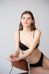 Model digitals (snapshots) for a modeling agency. A young female model stands in front of a plain white background, wearing black lingerie and heels. Natural light, neutral pose, minimal makeup