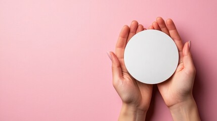 This image features two hands gently holding a circular white object against a soft pink background, emphasizing simplicity and purity in design.