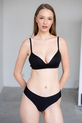 Fototapeta premium Professional modeling digitals of a young female model in black lingerie, standing confidently in a clean studio setting. Capturing natural beauty, symmetry, and elegance for agency submission
