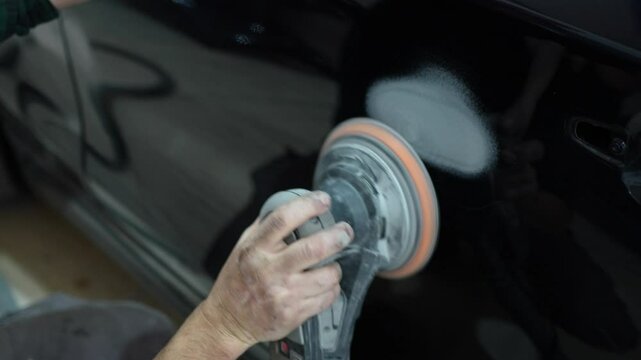 Auto body worker polishing car door with electric buffer in workshop
