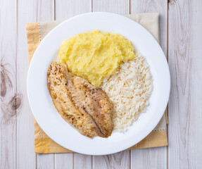 Grilled tilapia or saint peter with rice and mashed potato over wooden table