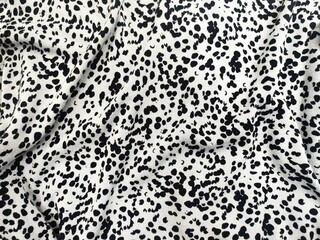 Background view of black and white spotted fabric with an abstract pattern resembling animal prints, featuring irregularly shaped dots on a textured textile surface with natural folds and creases.
