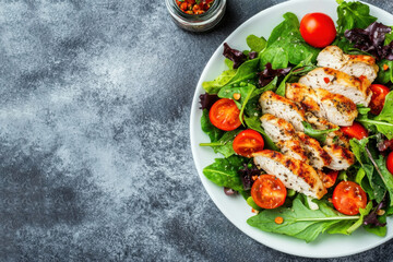 Appetizing summer salad with meat, tomatoes, basil, pepper and various herbs, healthy summer breakfast in a white plate, on a gray background, healthy eating concept, top view, space for text
